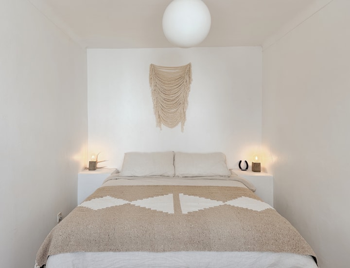 Dhoma kryesore e gjumit në Casa Corazon në The Blanco Bungalow Ericeira, me një krevat me madhësi King me dyshek krejt të ri, çarçafë dhe shtroja premium, komodinë dhe pamje nga kopshti. @blancobungalow