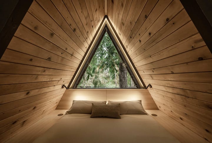 A King-sized loft bed with a memory foam mattress, luxury linen blend bedding, and multiple pillow options for the perfect sleep. Wireless chargers are within reach for added convenience. Sleep under the stars with the large window! 