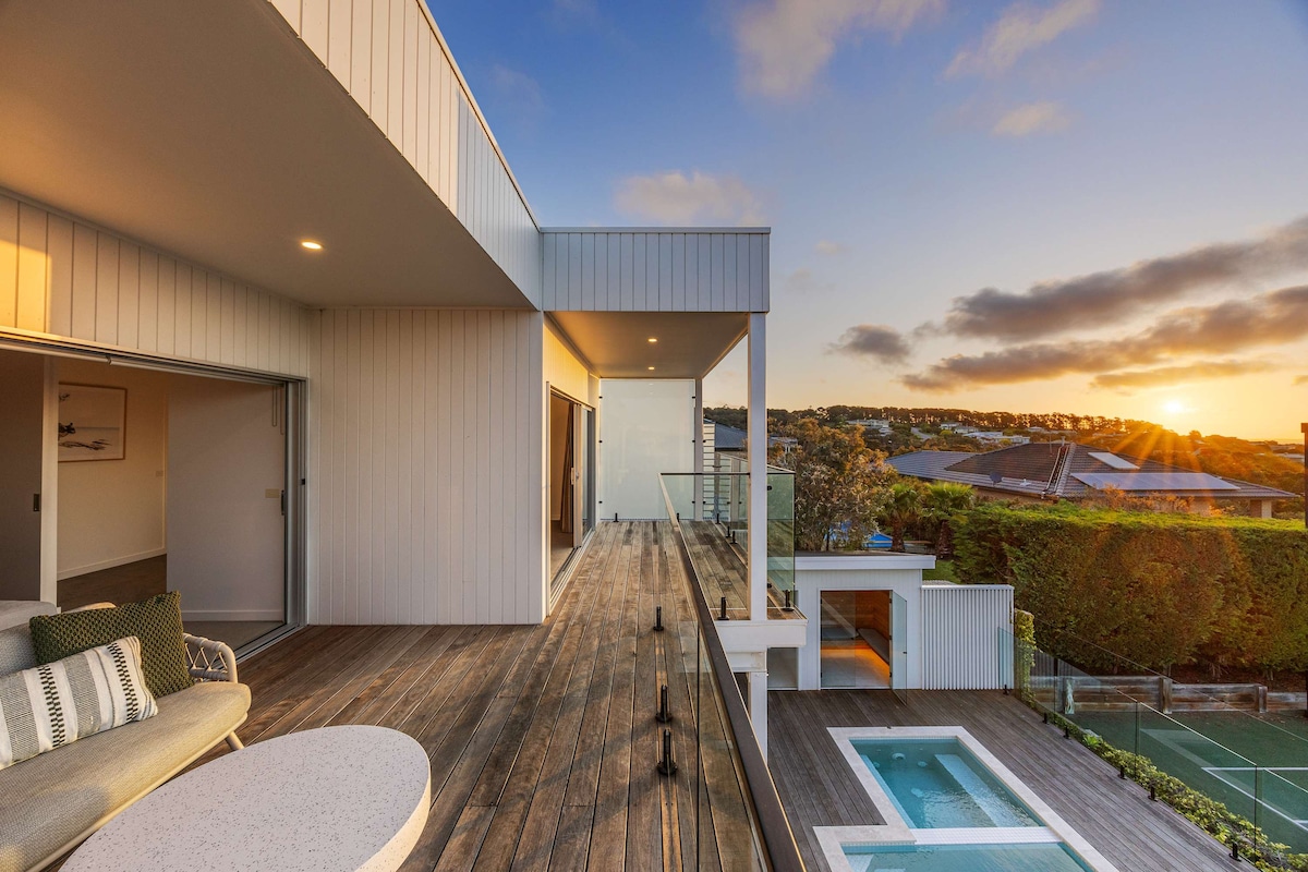 A spacious outdoor deck showcases a private pool surrounded by sleek tiles. The area is highlighted by contemporary seating and expansive glass doors that connect to the interior rooms. A picturesque sunset casts a warm glow over the surrounding landscape.