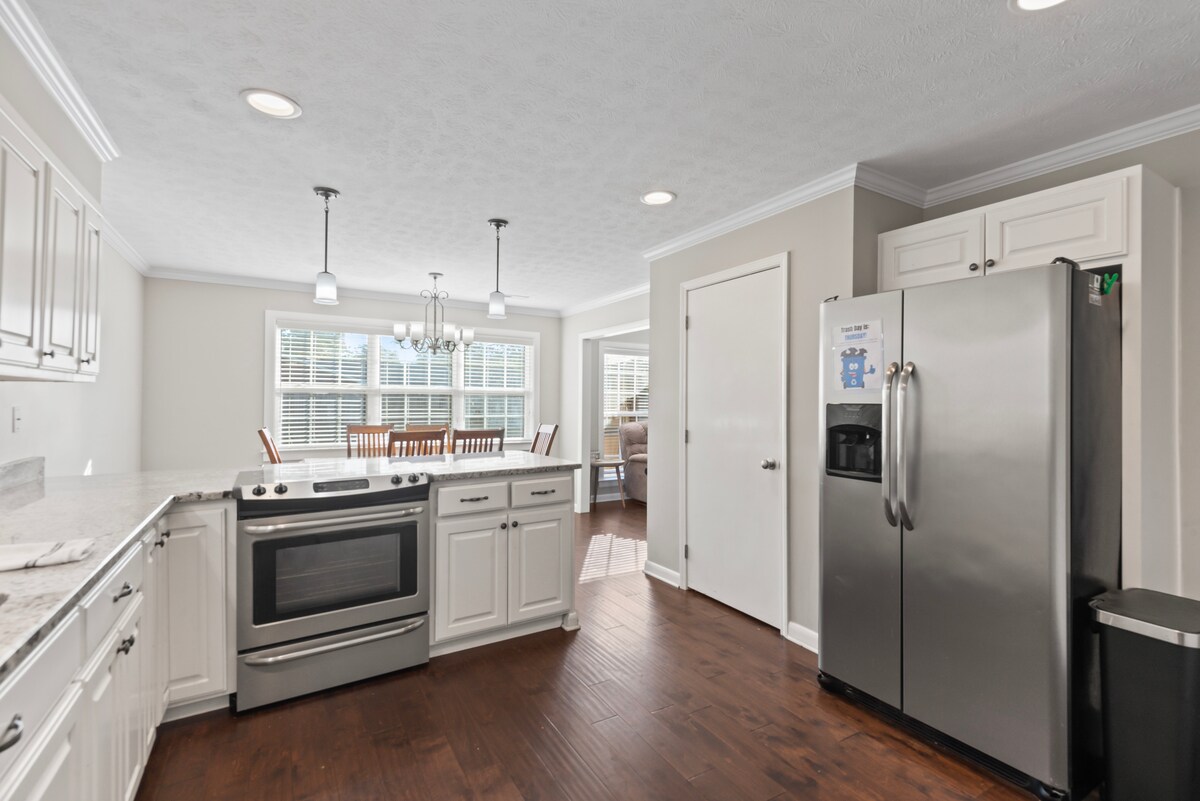 The kitchen is equipped with modern appliances including a stainless steel refrigerator and range. Ample cabinets are featured, along with a countertop providing extra prep space. Natural light floods in through large windows, enhancing the welcoming atmosphere shared with an adjacent dining area.