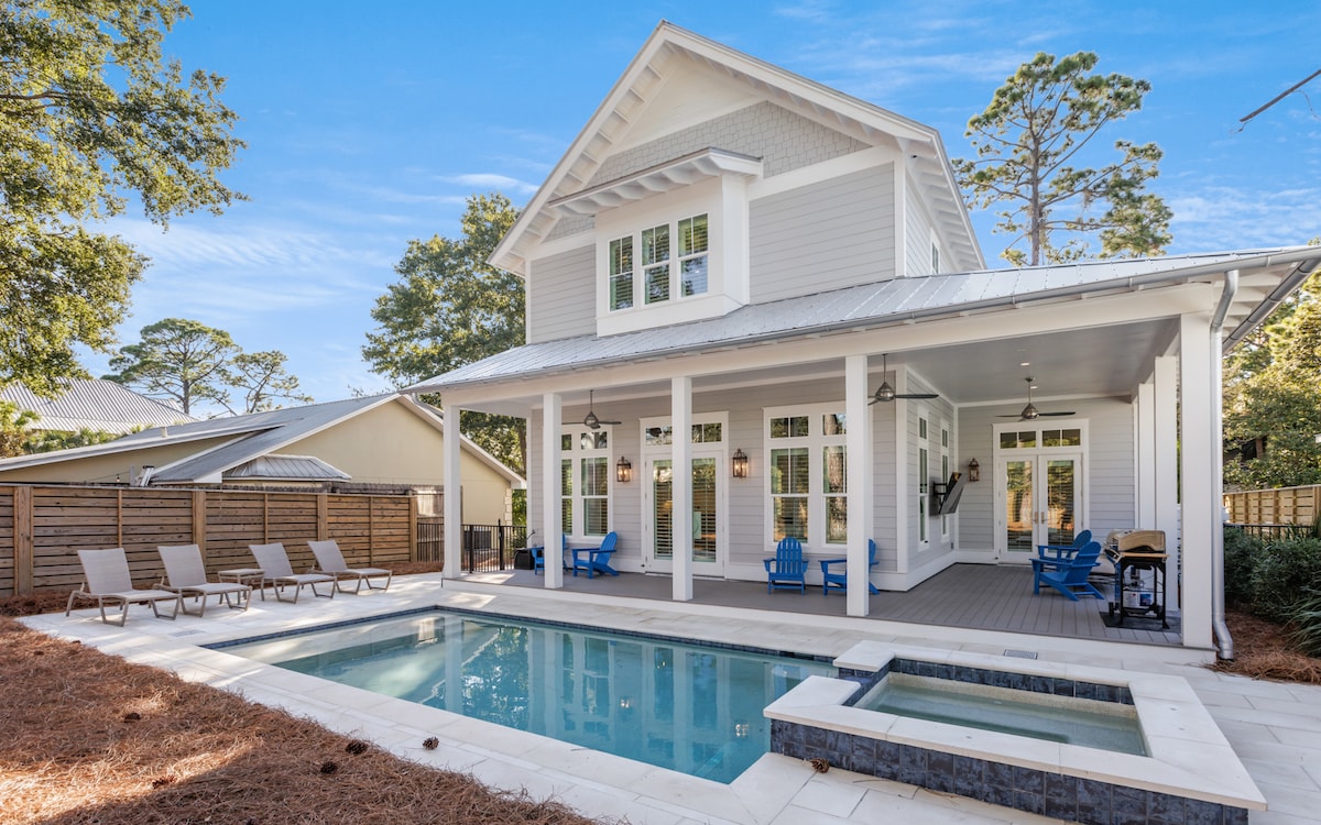 The exterior of the home features a modern design with a spacious covered porch and large windows. A rectangular pool with an attached spillover spa is surrounded by lounge chairs, creating an inviting outdoor retreat under a clear blue sky.