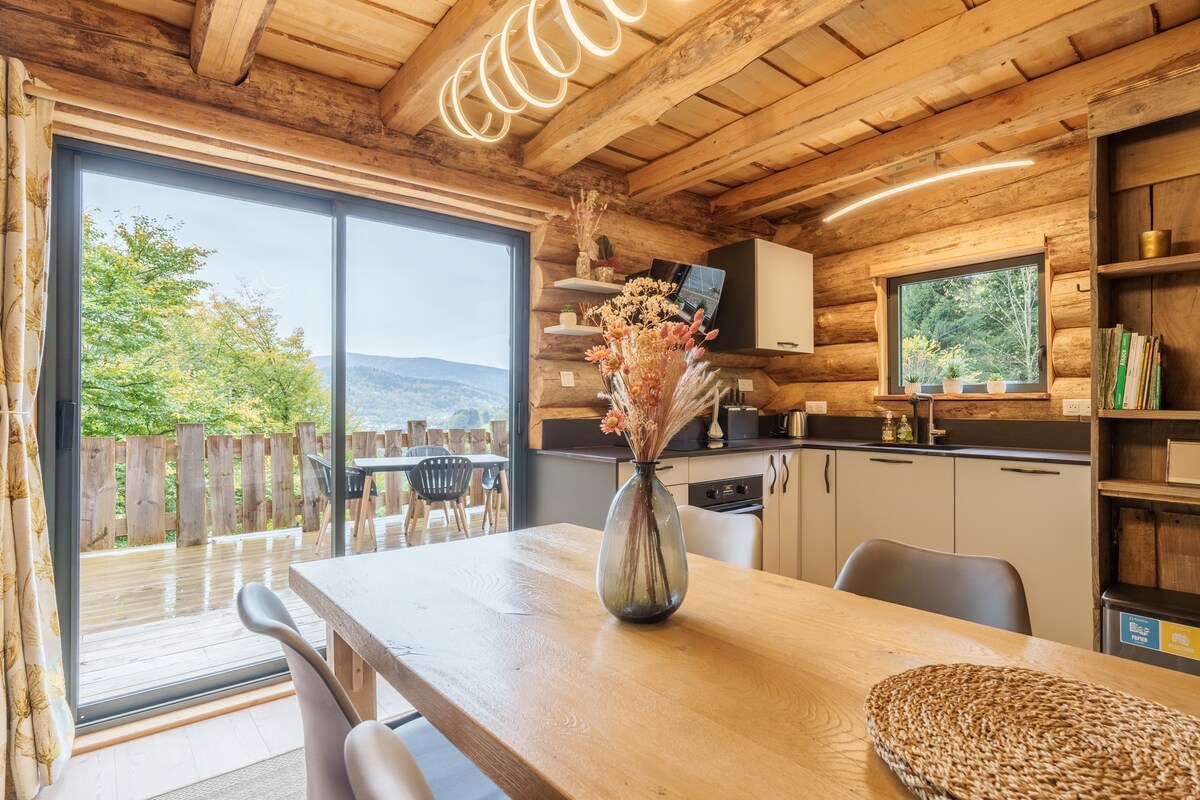 A seamless connection to nature is illustrated through large glass doors in the living area, leading to an outdoor deck. A rustic wooden table is set in the foreground, complemented by neutral-toned dining chairs and natural decor, enhancing the overall ambiance.