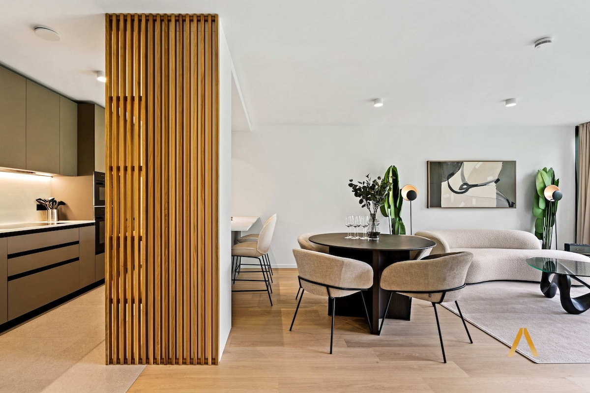 The open-concept living area features a modern kitchen blended with a dining space. Stylish furnishings include a round table surrounded by elegant chairs, and a cozy sofa, while natural light enhances the welcoming ambiance.