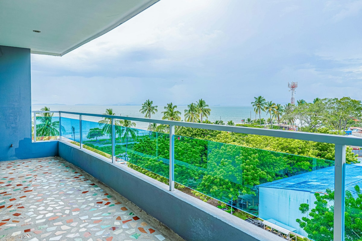 A private balcony offers partial views of the sea and surrounding mangroves, with expansive glass railings allowing for unobstructed sightlines. The floor features a decorative terrazzo finish, complementing the vibrant greenery below.