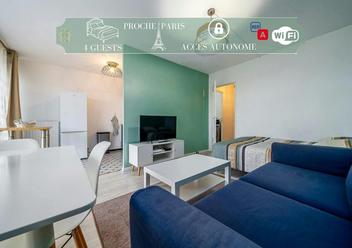 A brightly lit studio space is featured, showcasing a blue sofa and a wooden dining table. A television is positioned in front of a green accent wall, while the kitchen area includes a white refrigerator. Natural light enters through large windows, highlighting the inviting atmosphere.