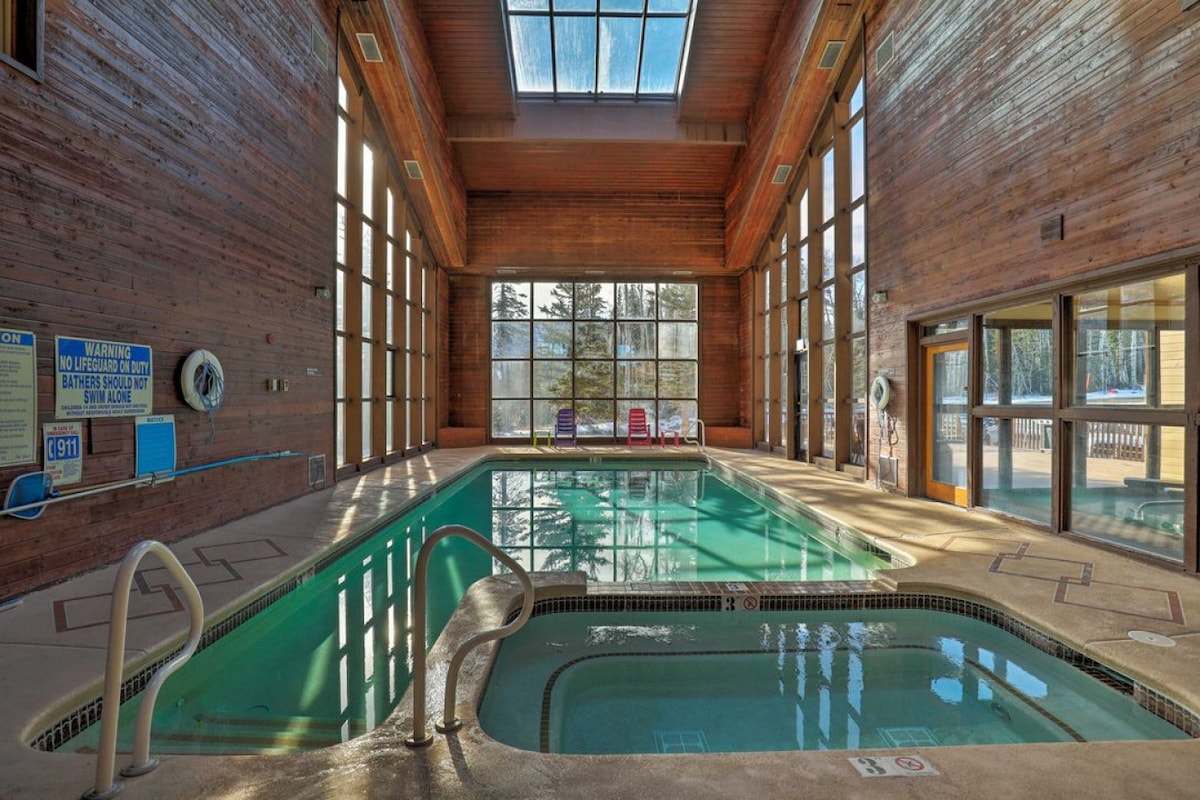 An indoor pool area is highlighted by large windows, allowing natural light to illuminate the space. The pool features a comfortable seating area with colorful lounge chairs positioned nearby. Natural wood accents and high ceilings enhance the warm atmosphere.