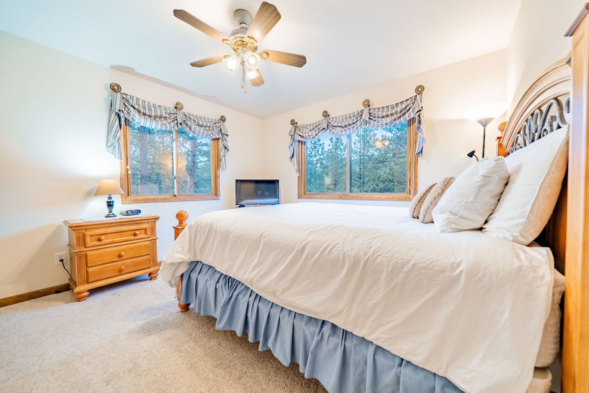 Spálňa s manželskou posteľou na poschodí s výhľadom na borovice