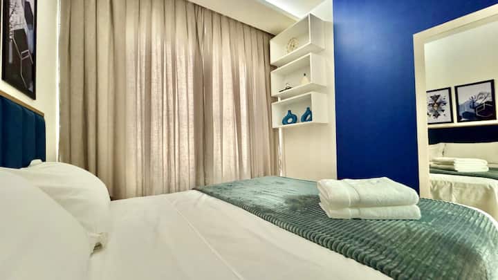 Dormitorio con un sofá verde claro, cortinas beige y una pared azul