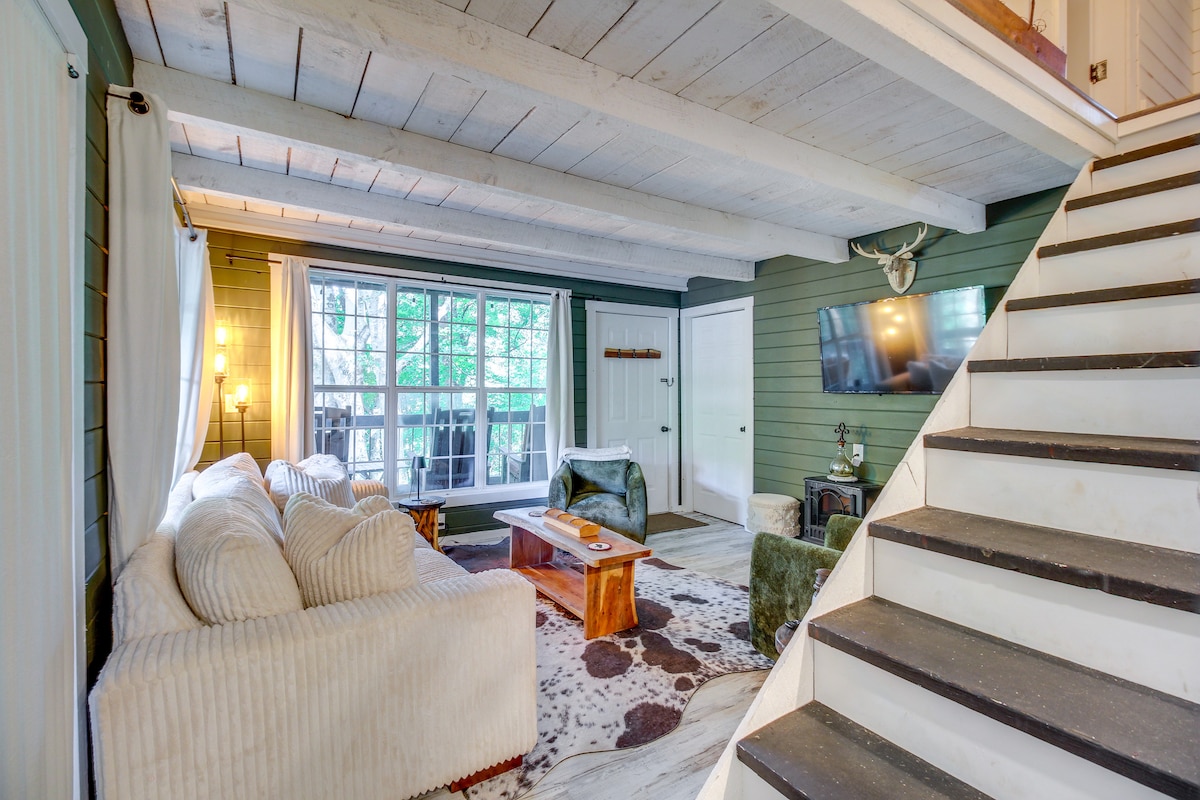 A welcoming living area features a light-colored sofa with textured upholstery and a striking wooden coffee table. Large windows allow natural light to fill the space, while a staircase leads to the upper floor. Soft wall colors provide a calming atmosphere.