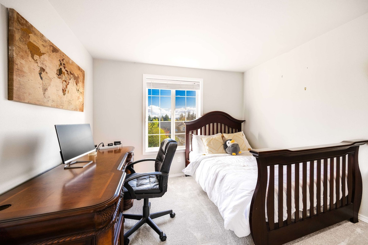 אזור שולחן עבודה מרווח עם מסך גדול וכיסא משרדי נוח, אידיאלי לעבודה מרחוק. החדר שטוף באור טבעי, ומציע סביבה מוארת ופרודוקטיבית.