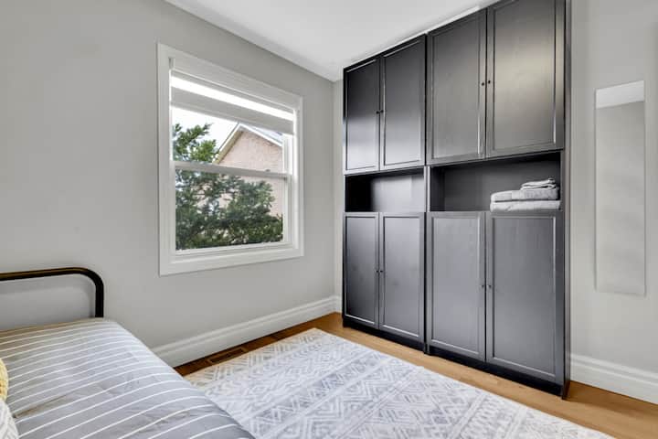 Светла и пријатна мала спална соба со дневен кревет, елегантен декор и голем прозорец кој нуди мирен поглед на отворено