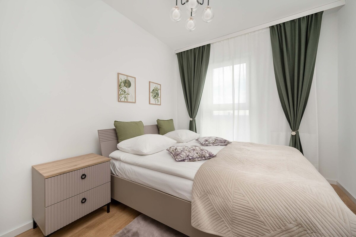 Kjo dhomë gjumi e rehatshme ka një krevat të madh me një mbulesë krevati me ngjyrë të çelët. Perdet e errëta jeshile në sfond shtojnë një ndjesi elegance.