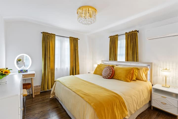 Dhomë gjumi king në katin e sipërm me krevat, dollap, komodinë, abazhurë USB dhe stacion grimi.