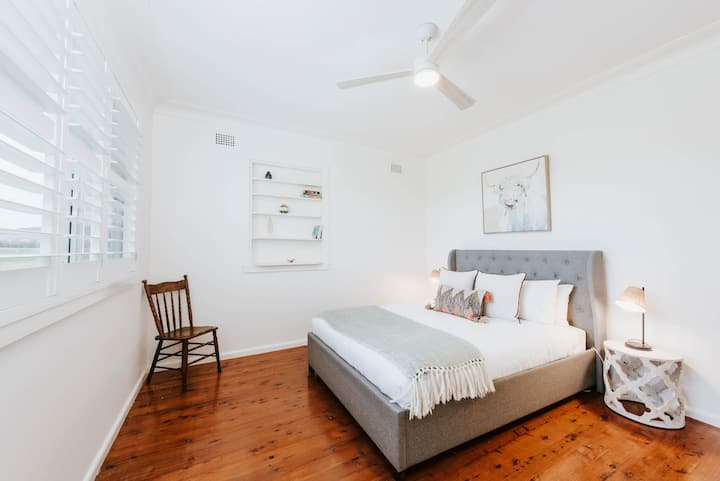 Уютно в двойното легло на спалня три, оградено с странични маси и лампи за четене. Вентилатор на тавана циркулира въздух за комфортен сън. 