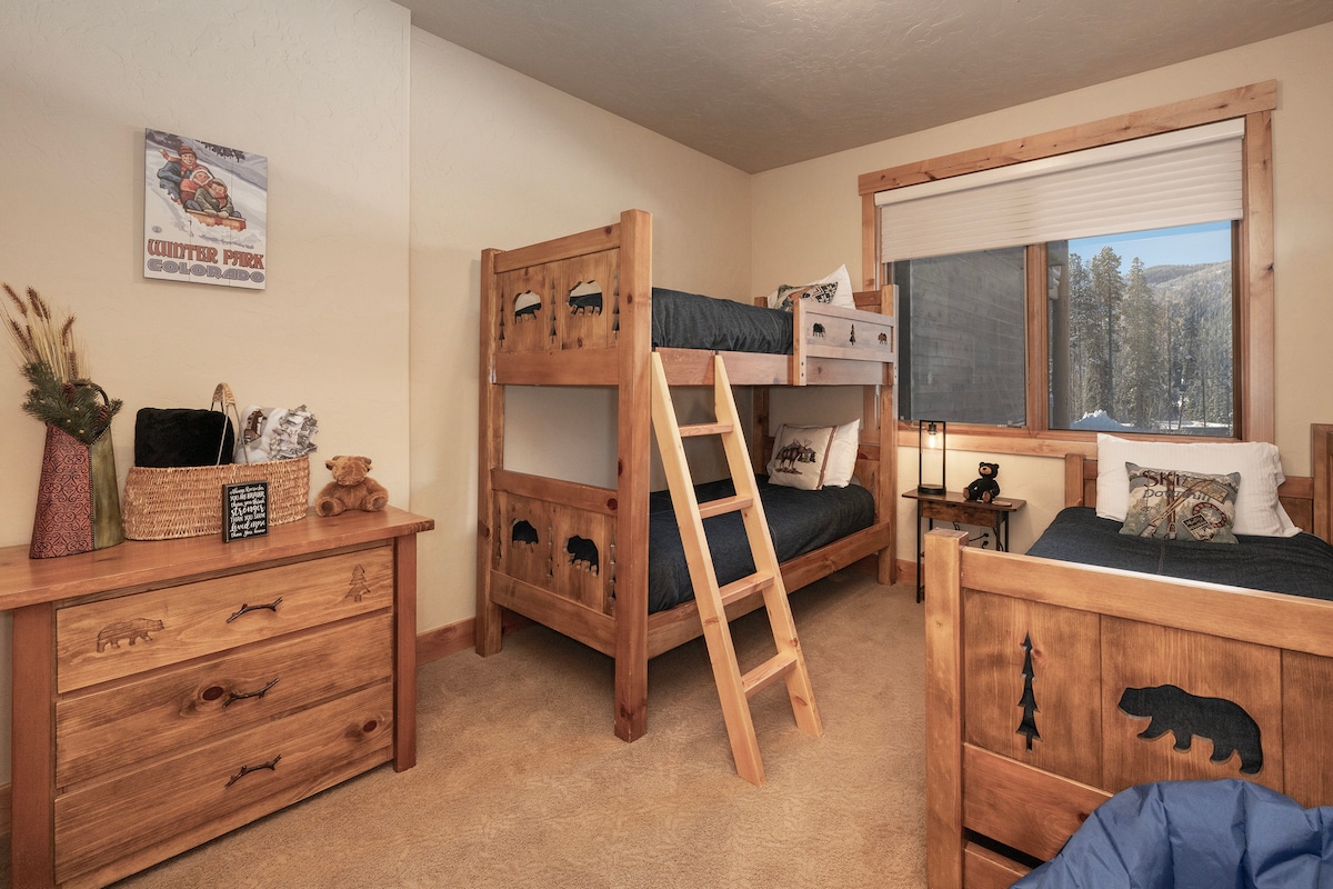 - Dormitorio con espejo de tocador y vistas al bosque de montaña.   - Muebles alpinos rústicos con detalles de madera natural.   - Cómodo estilo lodge para noches de montaña tranquilas.