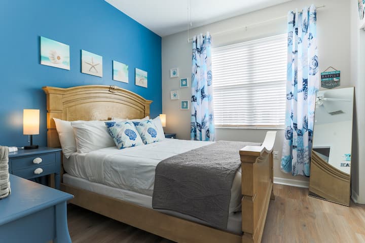 Junior Suite - Cozy Retreat Suite featuring a queen bed and a convenient workstation. This beach-themed room offers a peaceful ambiance with soft, beach-inspired decor, creating a relaxing space for both rest and productivity.
