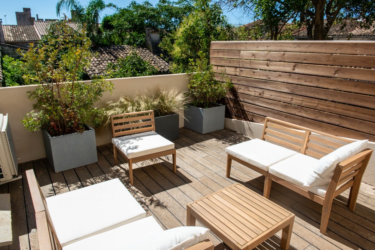 An outdoor terrace is featured, highlighting wooden decking and comfortable seating arrangements. Soft cushions adorn the seating, and planters filled with greenery enhance the natural ambiance. A wooden privacy screen adds an element of seclusion, complementing the urban surroundings.