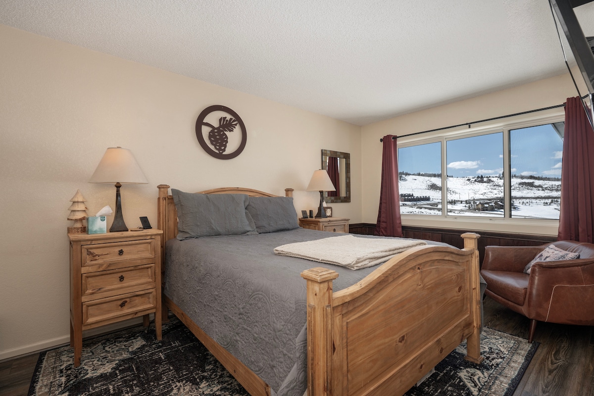 Удобна рустикална спална соба со рачно изработен мебел од дрво каде што ќе се разбудите со прекрасен зимски поглед кон планините преку вашиот прозорец.