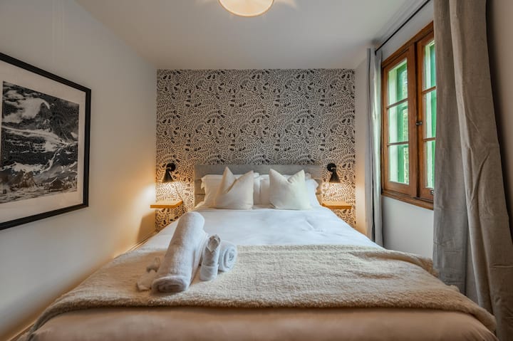 Un dormitorio acogedor y luminoso con una cama tamaño queen, papel tapiz colorido e iluminación natural suave.