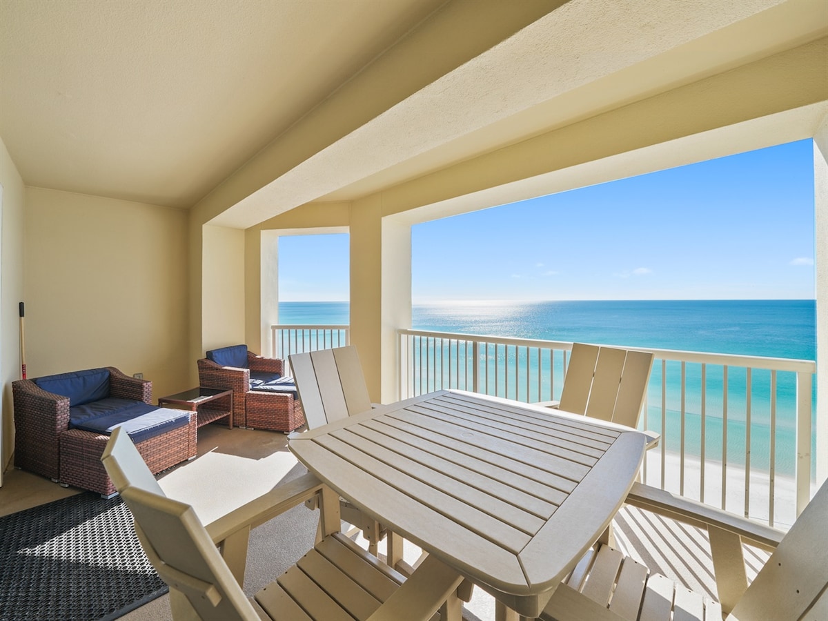 A spacious balcony offers unobstructed views of the Gulf waters. Comfortable seating is provided by wicker chairs and a modern table, inviting relaxation. The calming blue sky complements the serene atmosphere, while the surrounding railings ensure safety and stability.