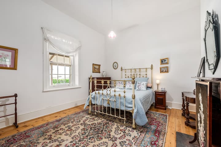 Une chambre classique avec un cadre de lit en laiton, des meubles vintage et des touches de bleu pâle.