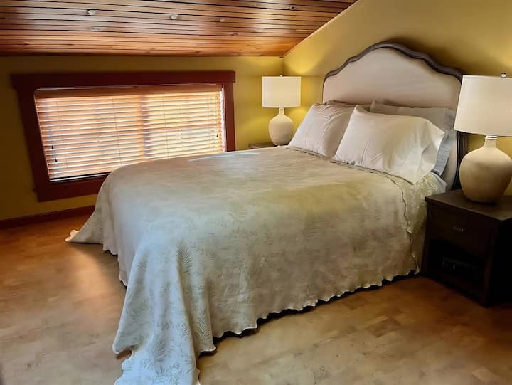 Veľká manželská posteľ s nočnými stolíkmi a lampami na oboch stranách. Strešné okno vnáša do izby ešte väčší charakter.