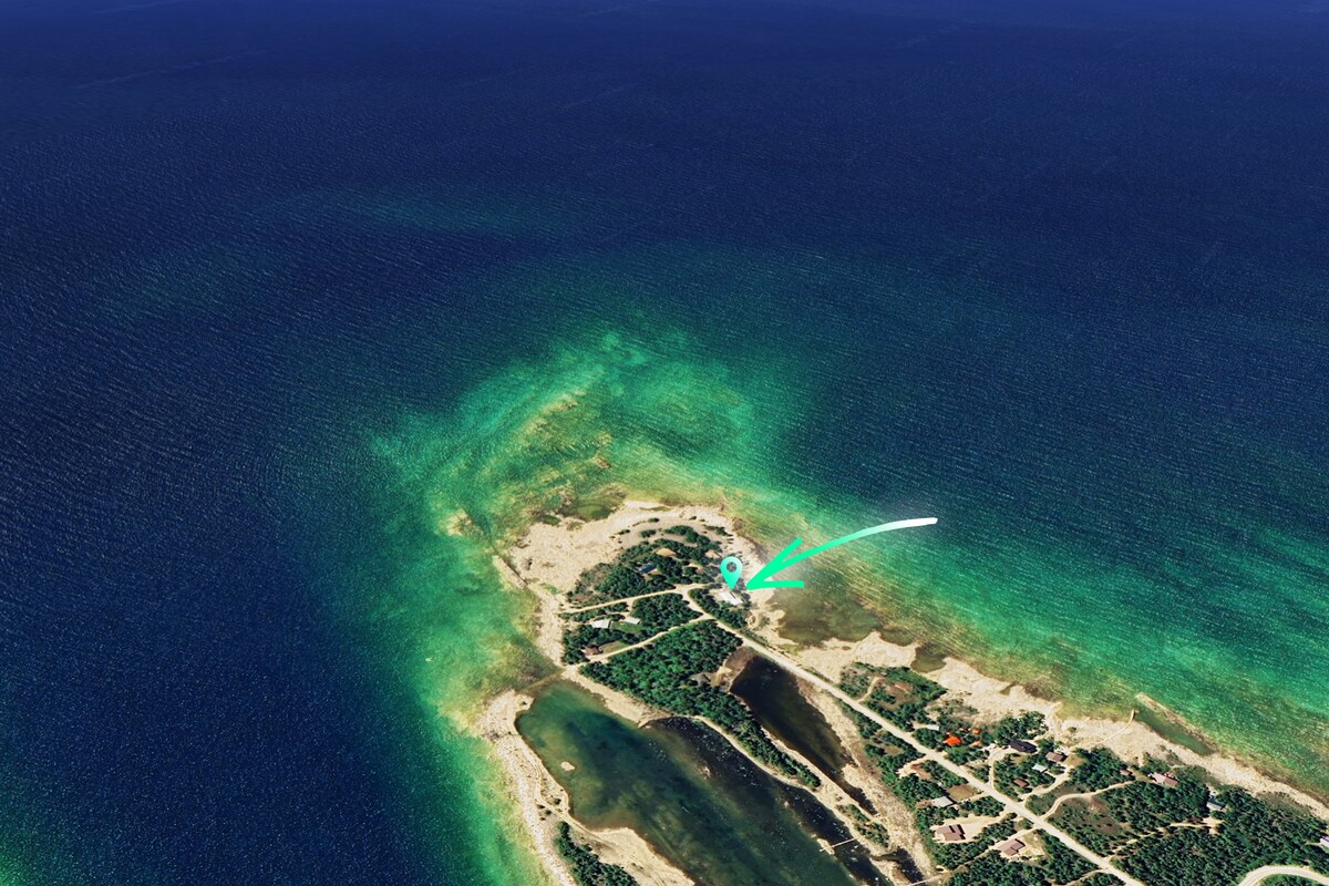 An aerial view of the northern Bruce Peninsula showcases the vibrant blue waters of Lake Huron. The shoreline is visible, surrounded by lush greenery and sandy areas, emphasizing the natural beauty of the coastal landscape.