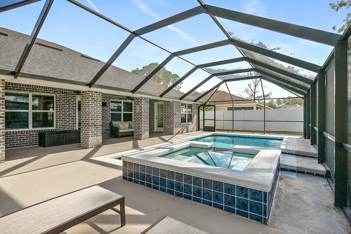 A screened-in patio features a private heated hot tub and saltwater pool, surrounded by modern outdoor furniture. The spacious deck includes comfortable lounge chairs, and large windows provide a view of the well-lit outdoor area and tranquil surroundings.