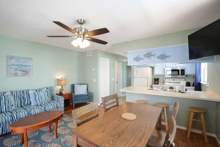 Útulná obývacia izba a jedáleň s pobrežnou výzdobou a otvorenou kuchyňou.
