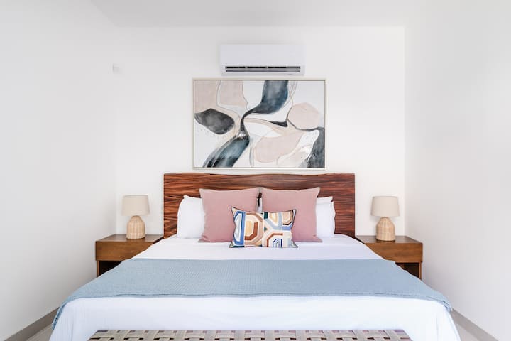 - Опуштете се во оваа мирна соба со кадифен кревет со руменило и сини тонови
- Природните текстури и модерната уметност додаваат топлина на чистата, бела палета
- Останете ладни и удобни со клима уред и меко амбиентално осветлување