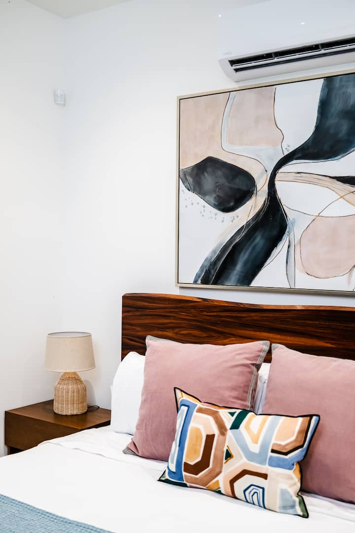 - Современите кривини и меките тонови во ѕидната уметност создаваат смирувачки визуелен фокус
- Мешавина од текстури од кадифени перници и дрвена рамка носи богат карактер
- Разбудете се удобно со удобна постелнина и малку смел стил