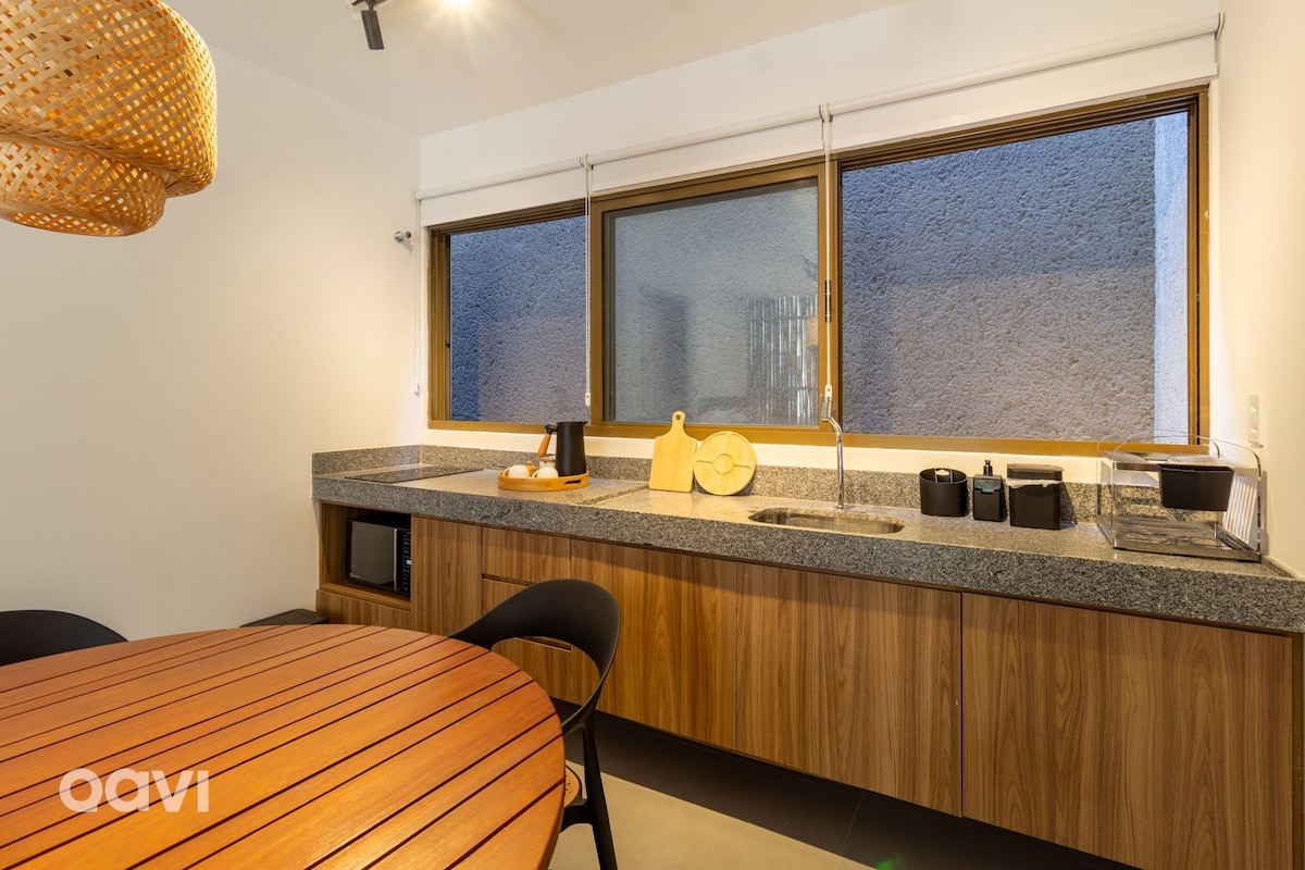 A modern kitchen area features a wooden countertop with decorative kitchenware and a sink. Large windows allow natural light to fill the space, while a round wooden dining table with black chairs provides a welcoming spot for meals.