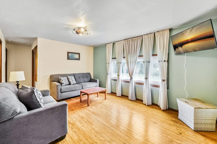 Acogedora sala de estar con luz natural, decoración moderna y un televisor montado en la pared, perfecto para relajarse.