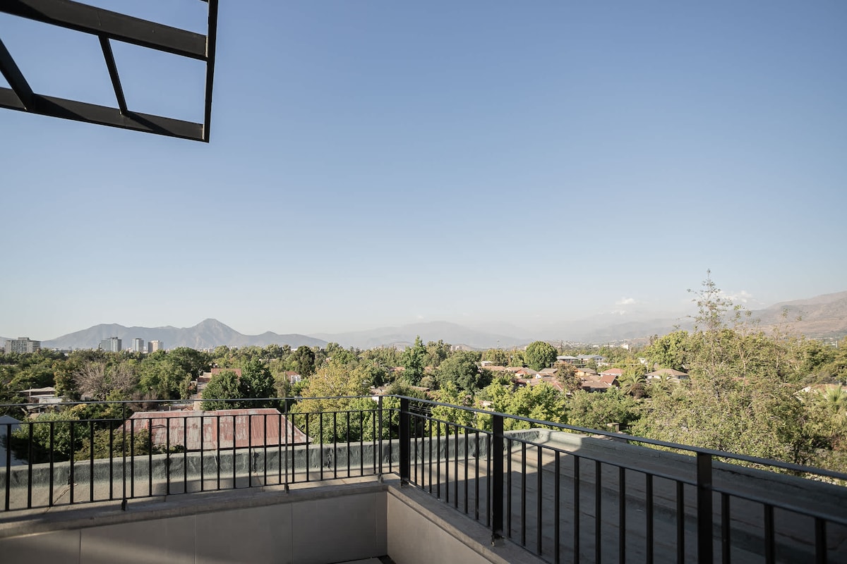 An expansive view showcases the surrounding greenery and distant mountains from the terrace. The clear sky creates a serene atmosphere, while the balcony railing adds a touch of modern design to the space.