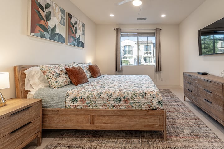 温馨的卧室，配有暖色调的木质家具、花卉装饰和壁挂电视