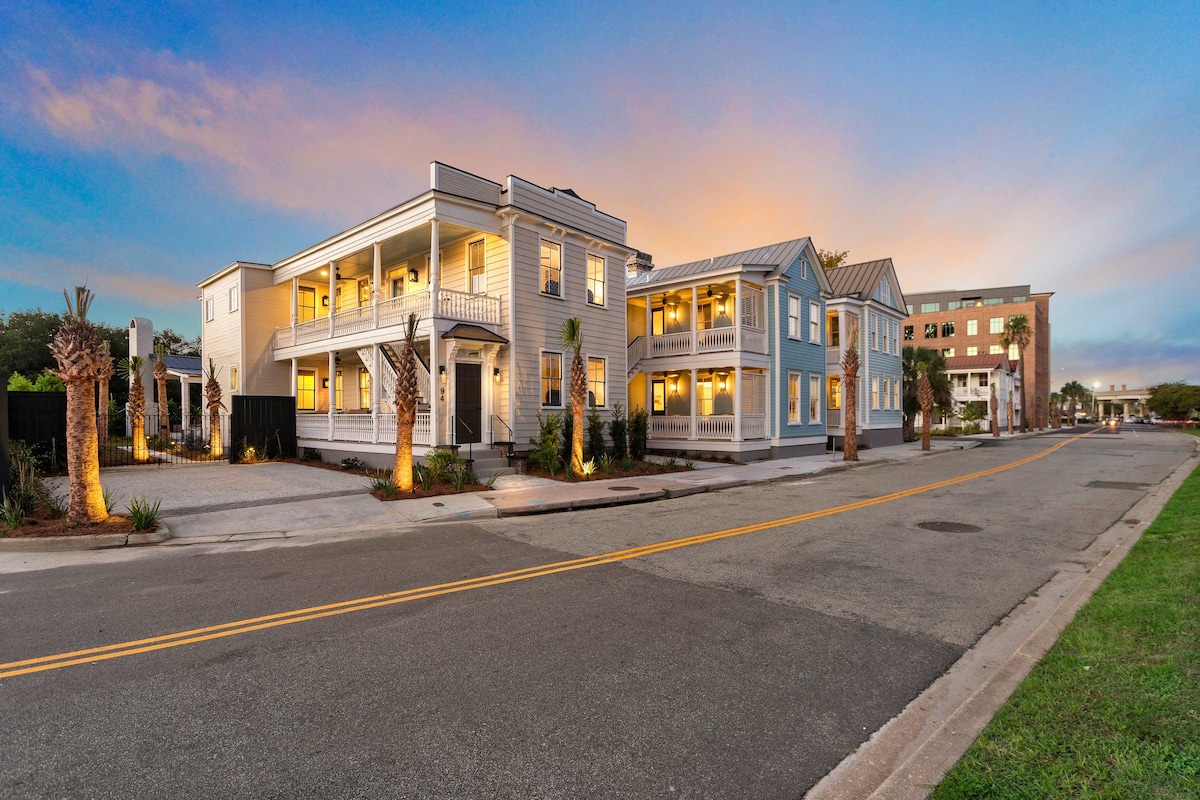 The exterior view captures a two-story building showcasing a classic design with a light-colored facade. Palm trees line the front, and warm outdoor lighting enhances the inviting appearance as the sun sets. A spacious driveway and sidewalk indicate accessibility.