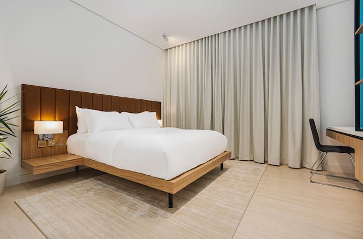 Área de dormir principal com estrutura de cama de madeira e paleta neutra simples.