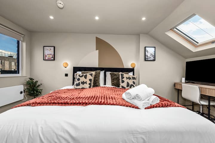 Acogedor dormitorio con una cama cómoda, un televisor, un escritorio y una ventana que deja entrar abundante luz natural, creando un espacio luminoso y acogedor.