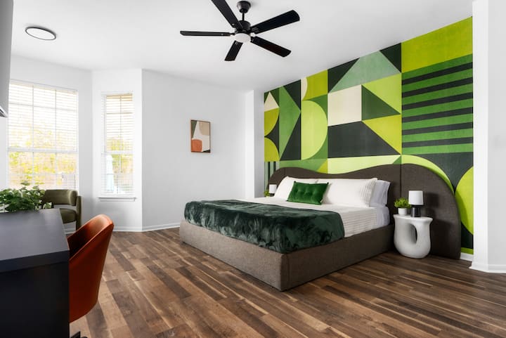 Relájate en este dormitorio espacioso y moderno, con una audaz pared de acento geométrico, una lujosa cama king y un acogedor espacio de trabajo para la mezcla perfecta de estilo y comodidad.