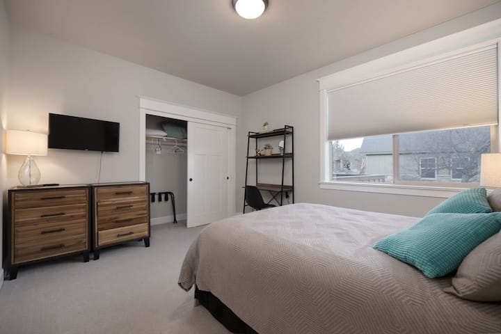 The first bedroom features a plush queen bed, desk, & smart TV