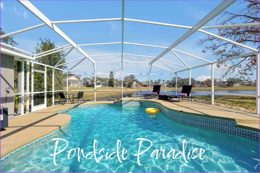 A serene outdoor space features a private saltwater pool with inviting turquoise water and a spacious deck area. Sun loungers are positioned around the pool, with a scenic view of the natural pond visible in the background under a clear blue sky.