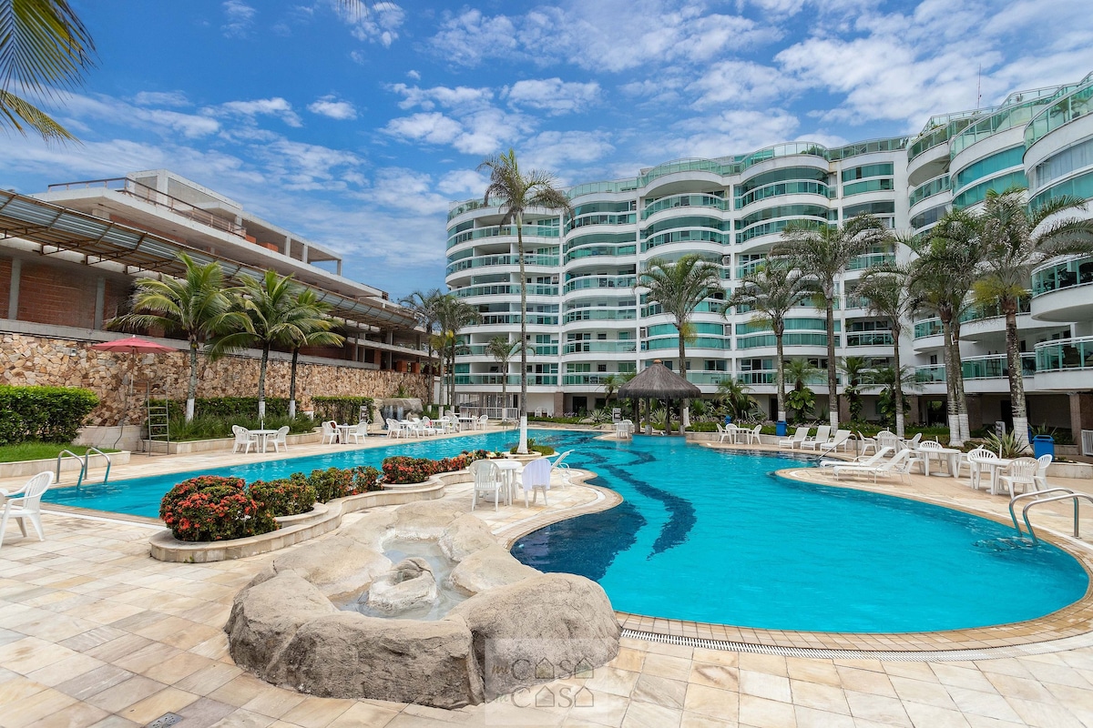 A spacious swimming pool is surrounded by palm trees and well-maintained landscaping. Lounge chairs are placed around the water, creating inviting spots for relaxation. The building features a modern architectural design with multiple levels, showcasing large windows that allow for natural light.