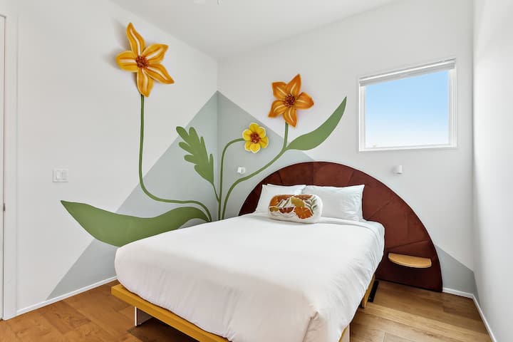 Bedroom 3: queen bed, downstairs, with a private en-suite bath. Art: Floating Flowers by Stronghold Studios, after Mardi Gras float flowers.