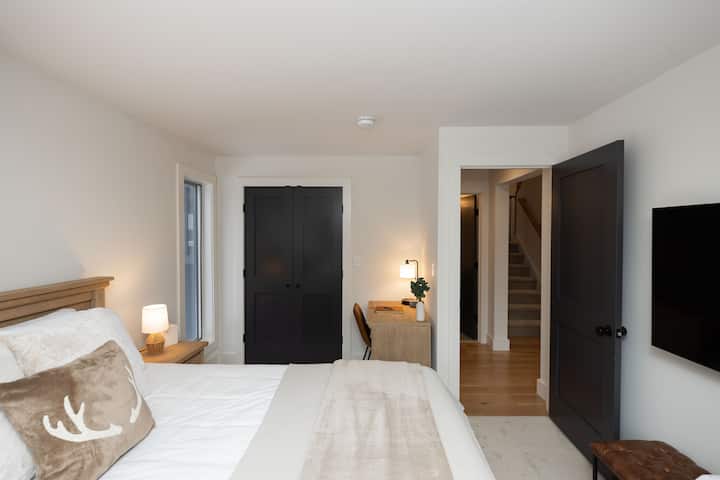 Dormitorio en el primer piso con cama tamaño queen, TV grande, escritorio y balcón con vistas al patio trasero sereno