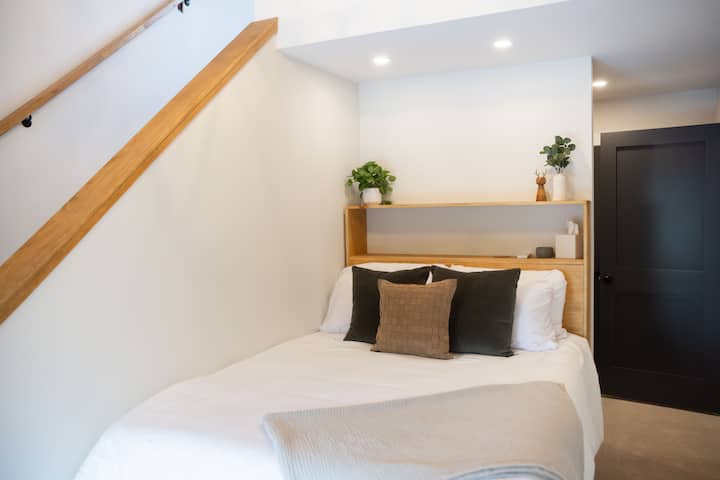 Dormitorio en el segundo piso con cama tamaño queen y escaleras que conducen a un loft con una acogedora cama individual