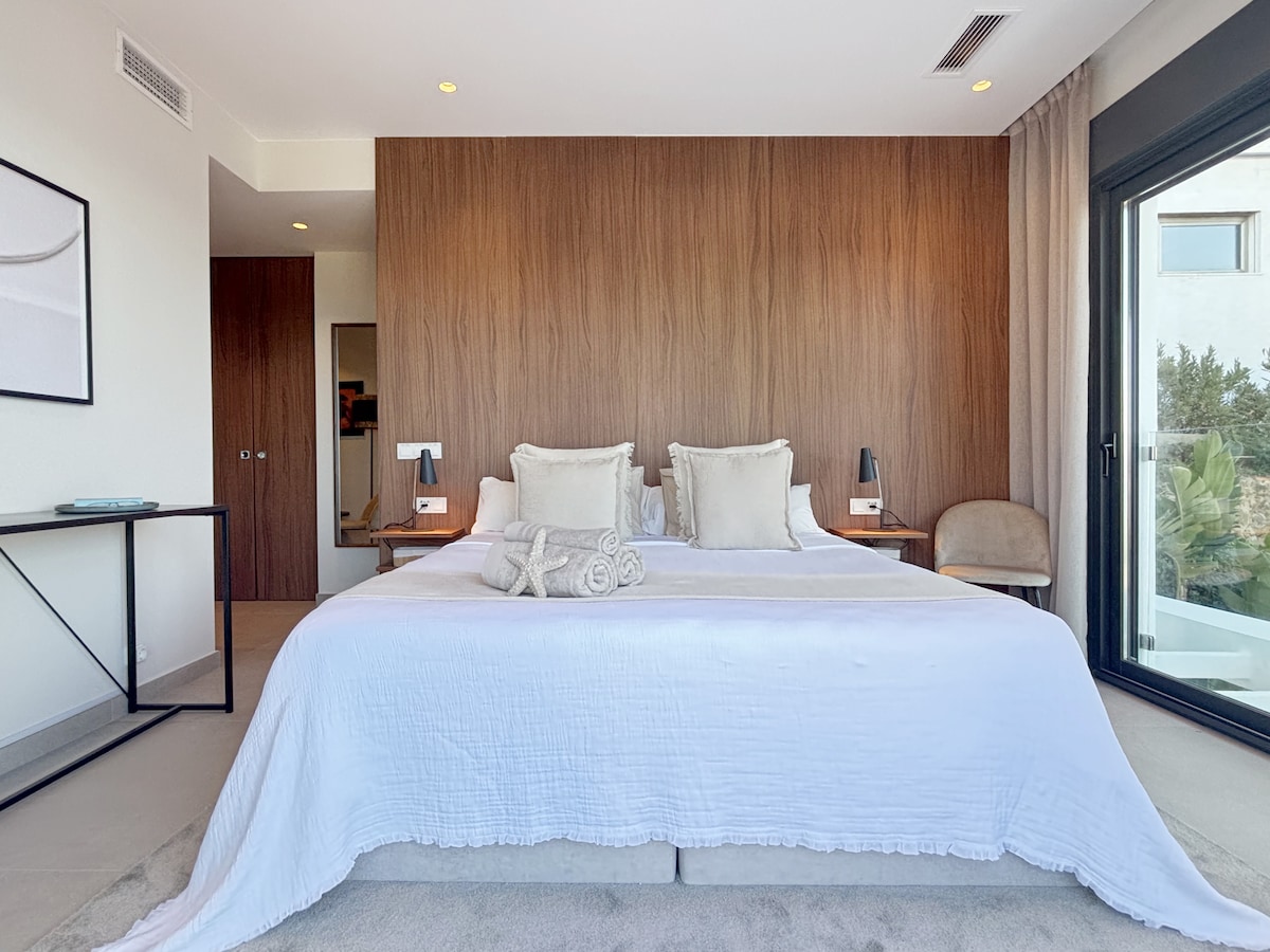 Dormitorio principal de diseño con una cómoda cama doble tamaño king. Incluye un cabecero de madera, iluminación ambiental, un amplio armario y una puerta corredera de cristal que proporciona mucha luz natural y acceso directo a la terraza. Climatización individual