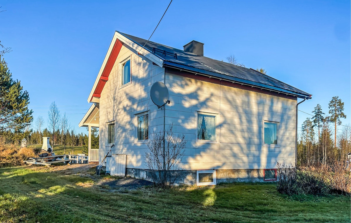 The side view of the accommodation highlights its light-colored exterior and sloped roof. Multiple windows allow natural light to illuminate the interior. Surrounding greenery and a clear blue sky create an inviting outdoor setting, enhancing the connection to nature.