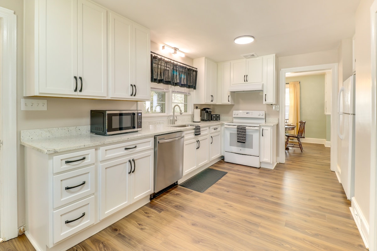 A well-equipped kitchen features white cabinetry and stainless steel appliances, including a refrigerator, stove, and dishwasher. A microwave is positioned on a counter, complemented by a window above the sink that allows natural light to brighten the space. The flooring is a warm wood laminate.