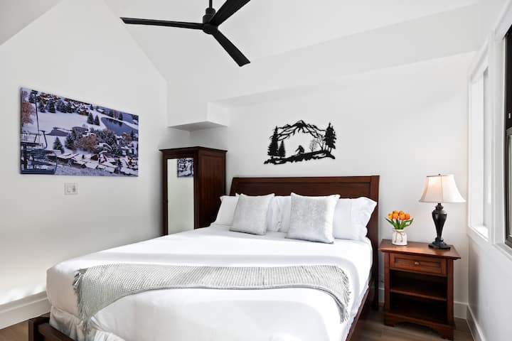 - Chambre avec cadre de lit en bois et décoration murale d'œuvres d'art enneigées  
- Draps blancs éclatants associés à des touches argentées et grises douces  
- L'éclairage chaleureux et la composition de tulipes ajoutent un charme de montagne confortable