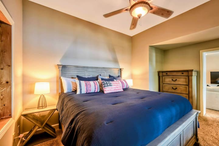Un dormitorio elegante y acogedor cuenta con una cama tamaño king con decoración de temática patriótica, iluminación cálida y ventilador de techo para mayor comodidad.